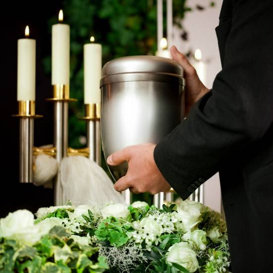 Grief – urn Funeral and cemetery death and dolor  - funeral and cemetery, mortician carrying the urn to a bed of white roses